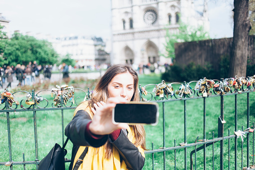 Young woman making selfie in front of padlock fence of Notre Dame de Paris. Focus on foreground.