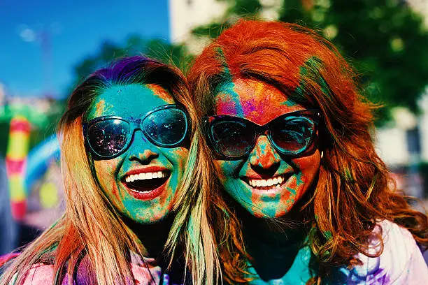 two friends portrait with colorful powder on their faces enjoying happy times in the holi color festival.
