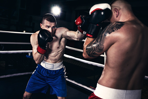 Portrait of Asian handsome sportsman wear boxing gloves in fitness gym. Attractive athlete male fighter workout and exercise by punching sand bag to maintain strong muscle and health care in gymnasium