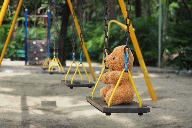 istock Teddy bear toy sitting alone on chain swing on kids playground 537851026