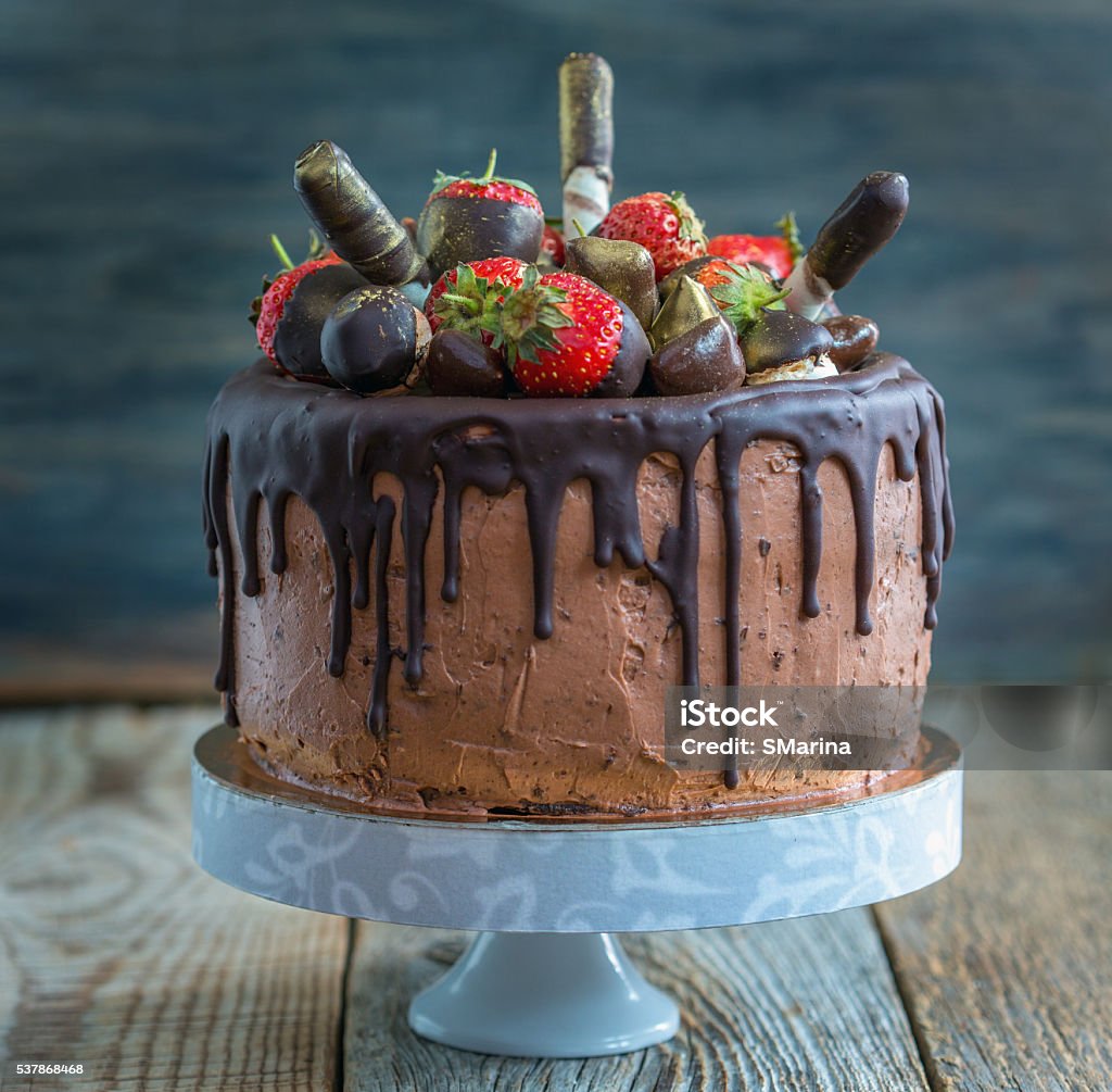 Chocolate cake with strawberries, wafer rolls and candies. Delicious chocolate cake with strawberries on a wooden table. Baked Pastry Item Stock Photo