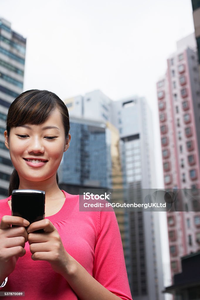 Businesswoman Reading Text Message On Cell Phone Beautiful young businesswoman reading text message on cell phone in front of buildings 2015 Stock Photo