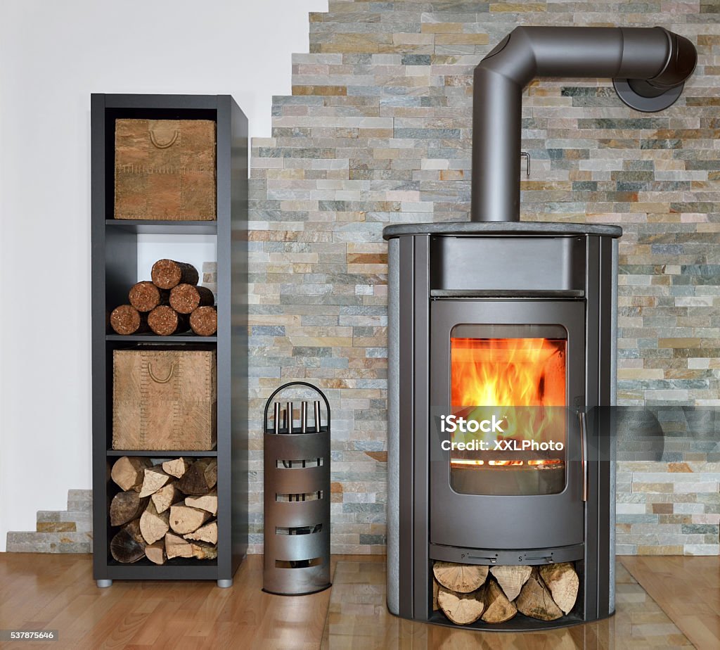 wood fired stove while burning wood fired stove with fire-wood, fire-irons, and briquettes from bark Wood Burning Stove Stock Photo