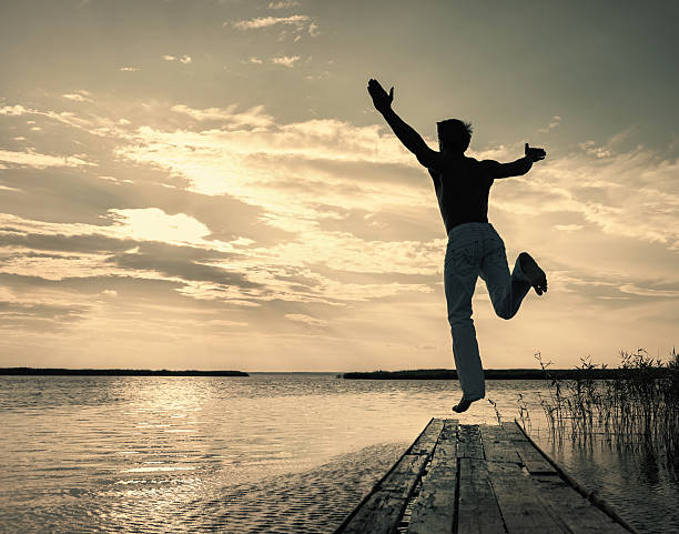 istock Man jumping up off small jetty at sunset 537880836
