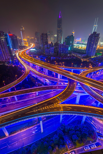 The futuristic neon lit highway and multi-layered Yan'an elevated interchange overlooked by the illuminated skyscrapers of Shanghai's Huangpu district glowing in the vibrant city night. ProPhoto RGB profile for maximum color fidelity and gamut.