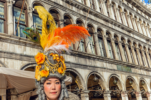 Venice, Italy - February10th, 2015: Portrait of Japanese woman in a mask, participant of the 2013 Carnival celebrations, posing for casual photographers and tourists in St. Mark's square.