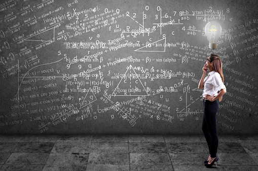 Side profile of a businesswoman solving mathematical equation on wall.