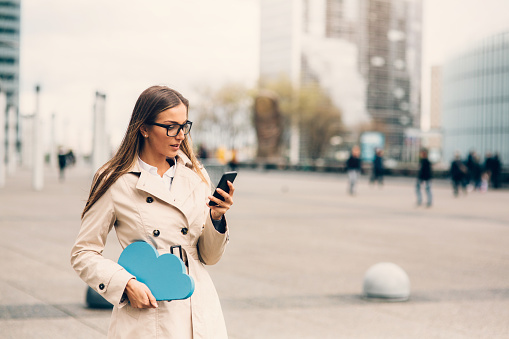 Businesswoman using a smart phone  and holding a big blue cloud on the street, 