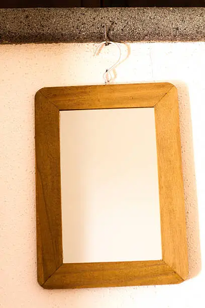 A rustic wood-frame mirror hanging on a hook. It looks also like an empty picture frame. Copy space available.