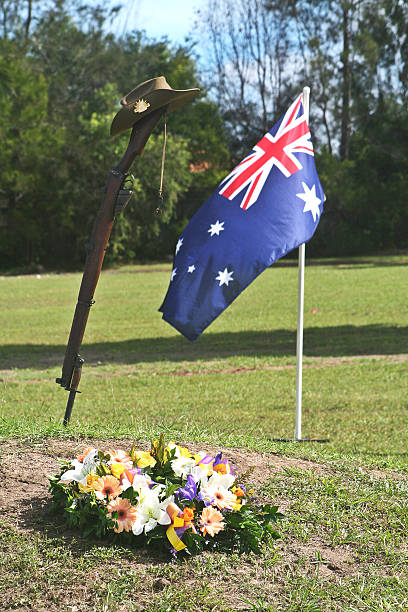 ANZAC Day Army Rifle, Slouch hat, Dogtags and Australian Flag Portrait shot (with room for copy) of an upturned, vintage Australian Army 303 rifle, a soldier's dogtags, floral wreath, slouch hat with an Australian Flag flying in the background during an ANZAC Day memorial service. larrikin stock pictures, royalty-free photos & images
