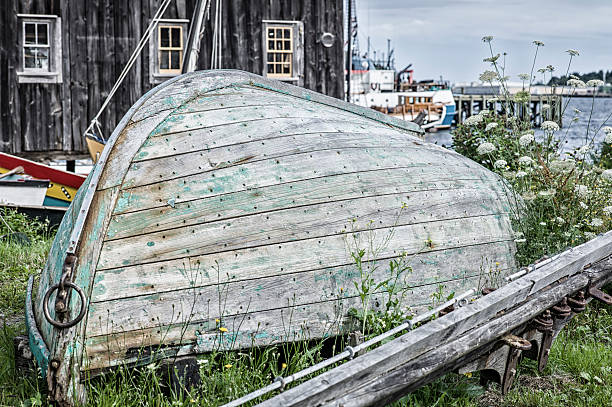 Old Boat on the Shore, Lunenburg, Nova Scotia.  Boat has faded paint and is upside down.  background is other boats and an old barn board shed.