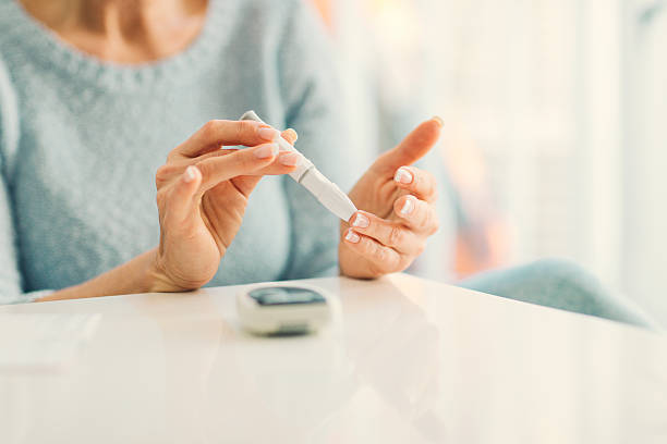 Mature Woman Doing Blood Sugar Test at home. Mature woman doing blood sugar test at home in a living room. Selective focus to her finger. body care stock pictures, royalty-free photos & images
