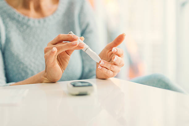 Mature Woman Doing Blood Sugar Test at home. Mature woman doing blood sugar test at home in a living room. Selective focus to her finger. blood sugar test stock pictures, royalty-free photos & images