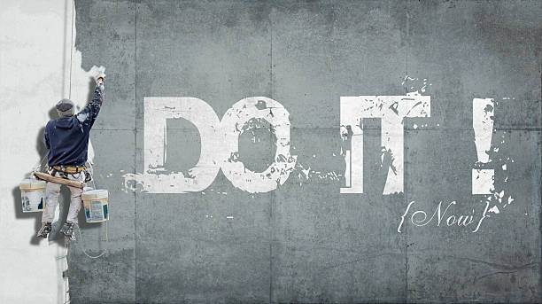 Do it now Painter hanging from harness painting a wall with the words do it now just do it stock pictures, royalty-free photos & images