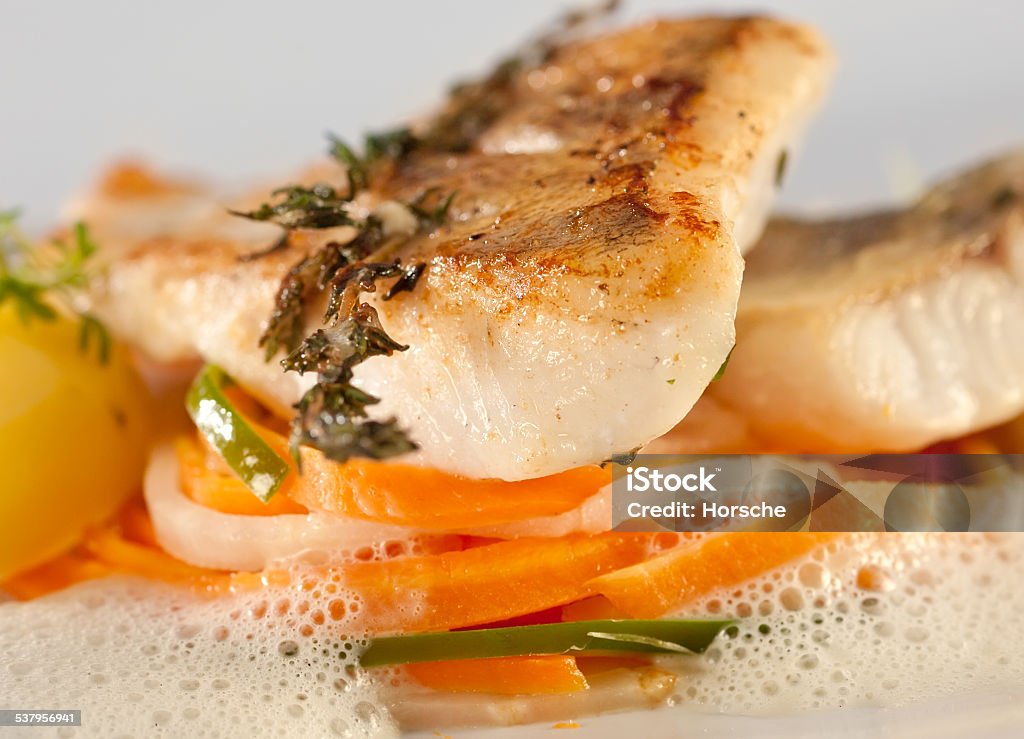 Fried pike perch fillet with vegetables. Fried pike perch with vegetables on a bed of thin sliced stripes of carrots, cucumber and asparagus in a fluffy sauce, served with potatoes. Plate Stock Photo