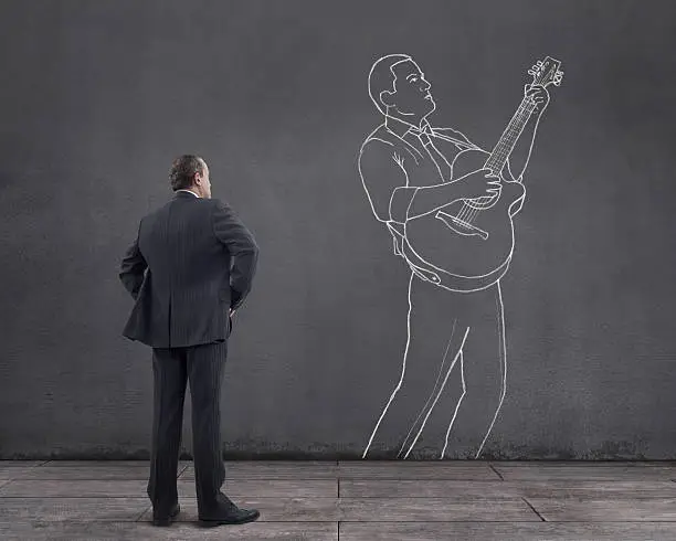 Rear view of businessman standing on wooden floor with businessman playing acoustic guitar sketched (chalk drawing) on the wall.
