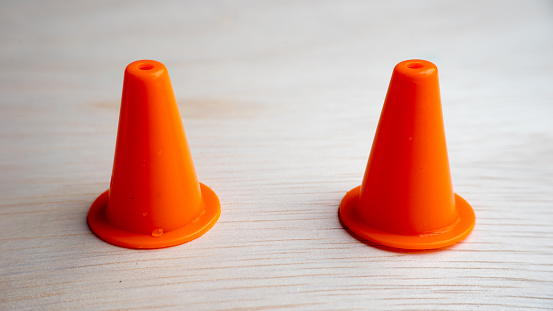 Multiple colour mini plastic safety cones on wooden surface. Slightly de-focused and close-up. Shot with natural light. Concept of work in progress. Copy space.