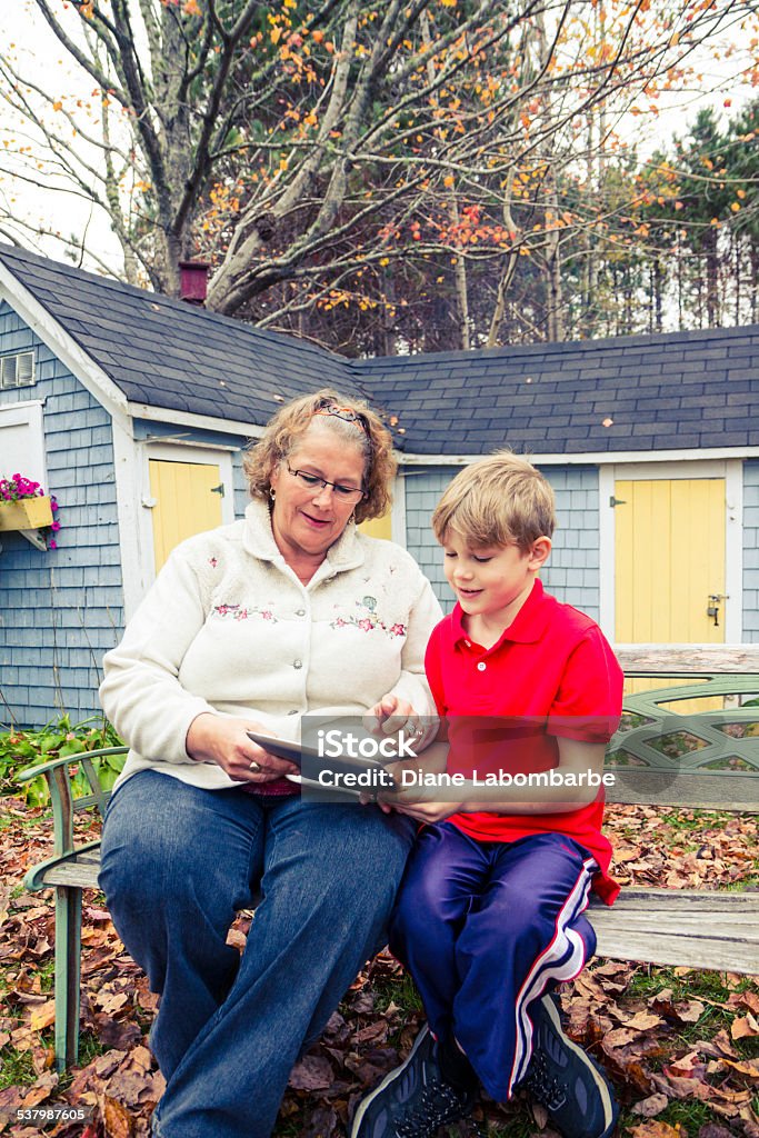 Grandmother Using A Tablet With Her Grandson Outside Autumn Stock Photo