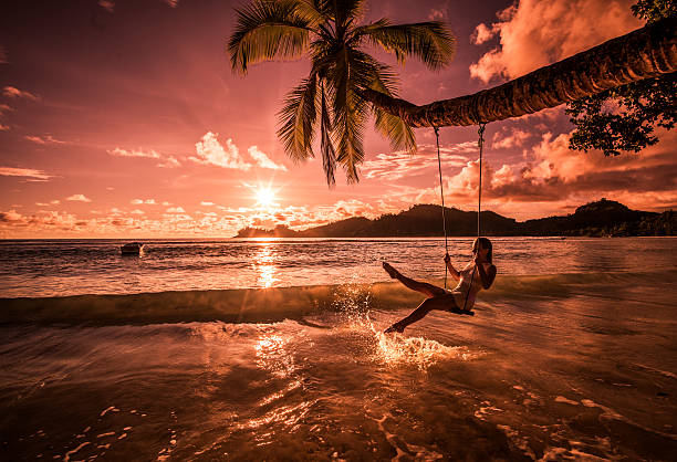 Carefree woman swinging above the sea at sunset beach. Young happy woman enjoying in beautiful sunset on the beach while swinging above the water and splashing it. sunset beach hawaii stock pictures, royalty-free photos & images