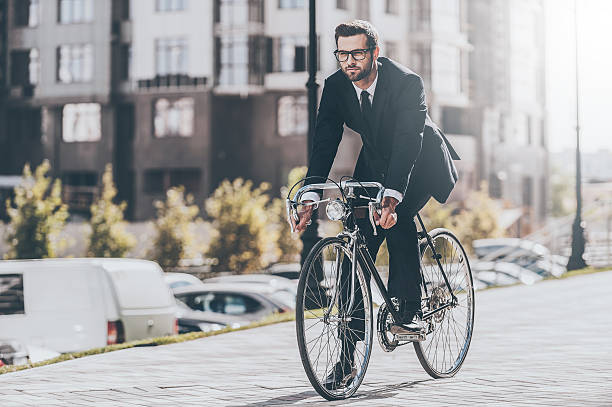 Cycling by the street. Full length of handsome young businessman looking forward while riding on his bicycle urbane stock pictures, royalty-free photos & images