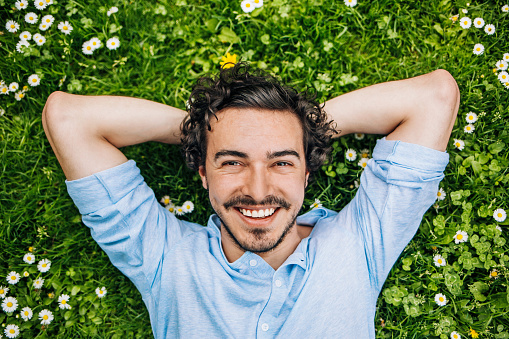Smiling young man lying down on a green grass with daisies