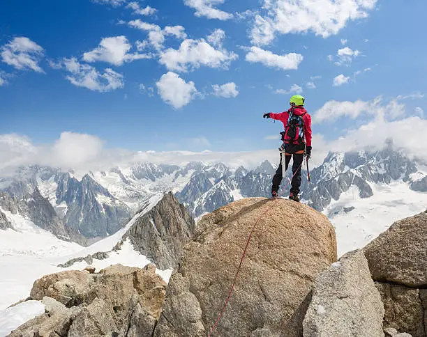 One male mountaineer on top of the mountain pointing his finger towards the Alps