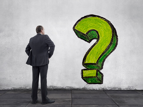 Rear view of businessman standing on sidewalk and looking at the hand drawn question mark painting on the wall. He is looking further, thinking, searching new ideas and way to exit.