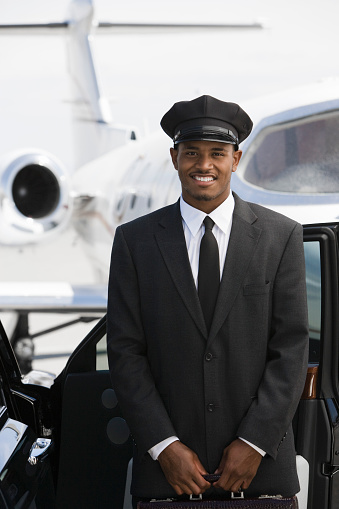 Portrait of mid-adult chauffeur standing in front of limousine and private jet.