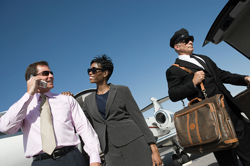 Mid-adult businesswoman, businessman and chauffeur in front of airplane on runway, low angle view.