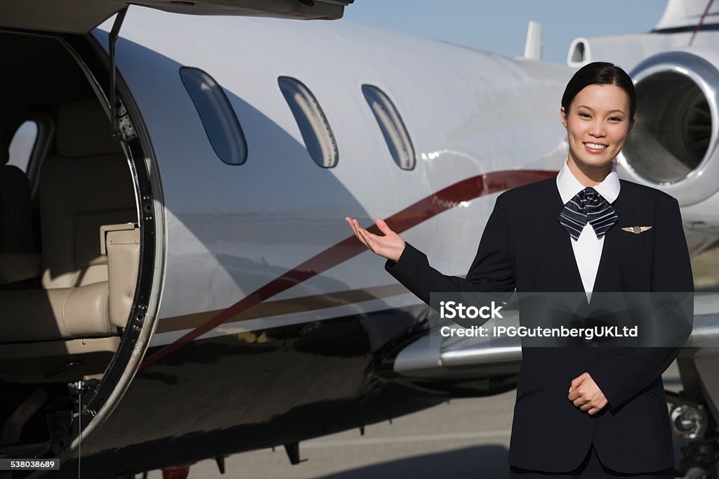 flight attendant in front of private jet Female Asian mid-adult flight attendant in front of private jet. 2015 Stock Photo