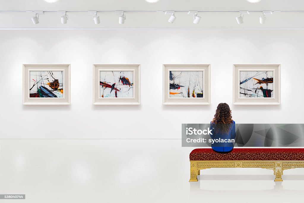 Young woman visits an art gallery In a exhibition centre, lonely young woman visits an art exhibition and watches artist's collection on the wall. Lightened white wall contains four white frames with artist's painting. Art Museum Stock Photo