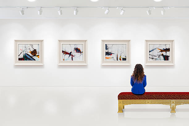 Young woman visits an art gallery In a exhibition centre, lonely young woman visits an art exhibition and watches artist's collection on the wall. Lightened white wall contains four white frames with artist's painting. museum stock pictures, royalty-free photos & images