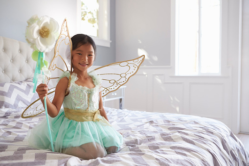 Girl Dressed In Fairy Costume Sitting On Bed At Home