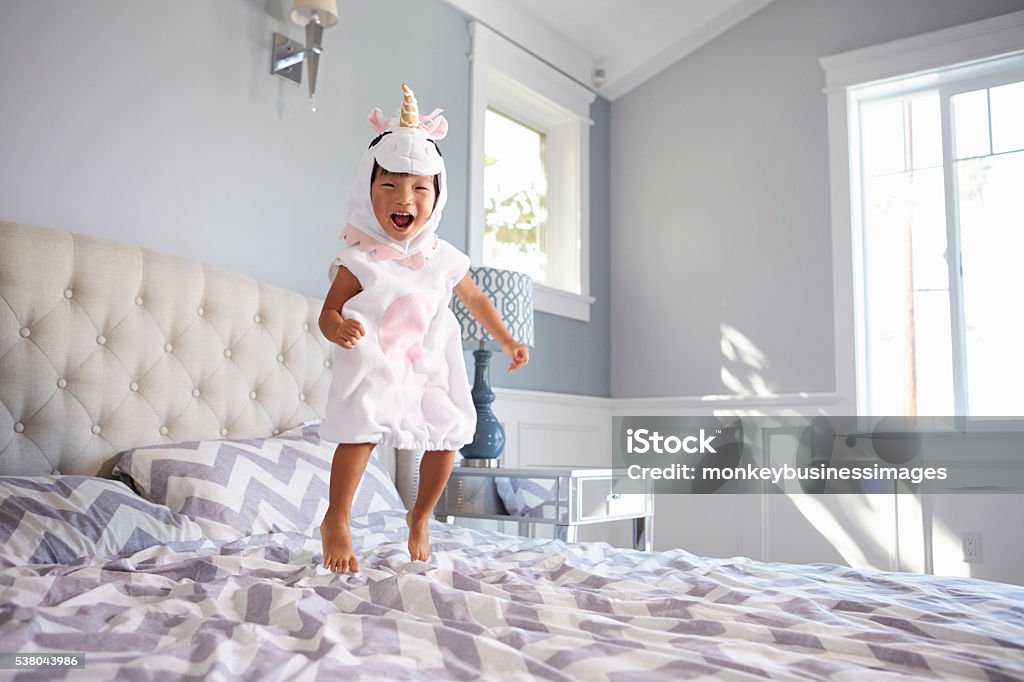 Chica vestido de Costume en Unicornio salto en la cama en su casa - Foto de stock de Niño libre de derechos