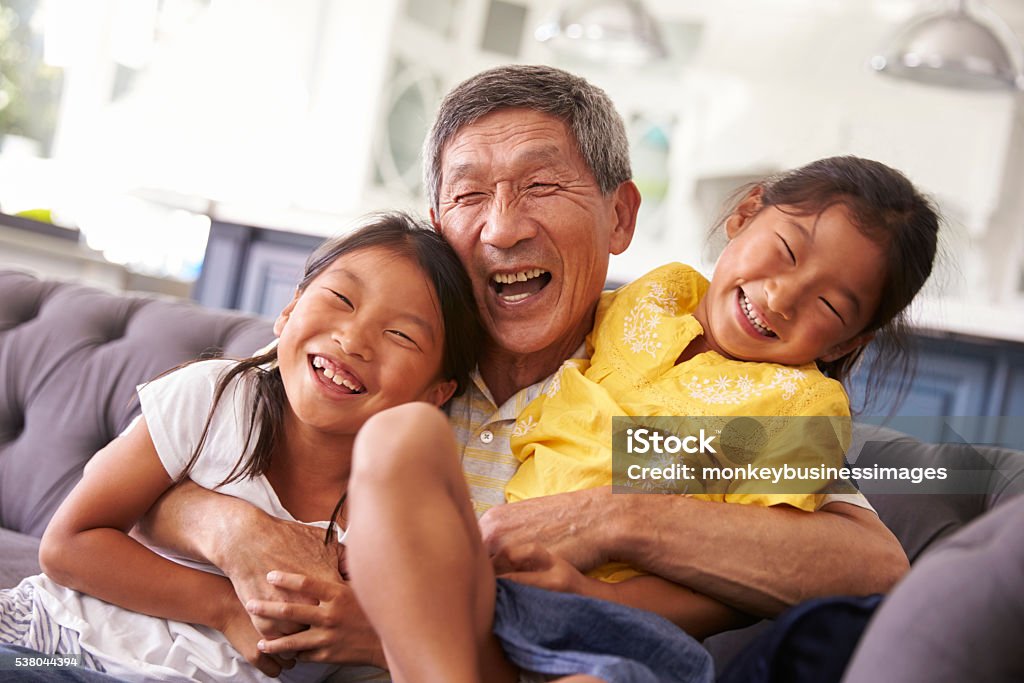 Grandfather And Granddaughters Relaxing On Sofa At Home Grandparent Stock Photo