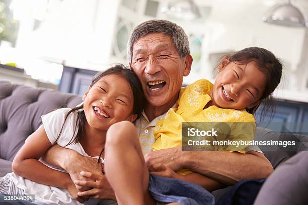 Grandfather And Granddaughters Relaxing On Sofa At Home Stock Photo - Download Image Now