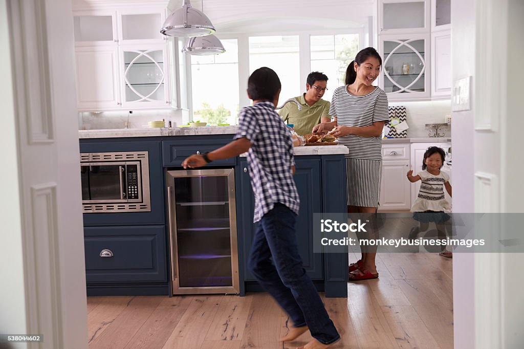 Parents Prepare Food As Children Play In Kitchen Family Stock Photo