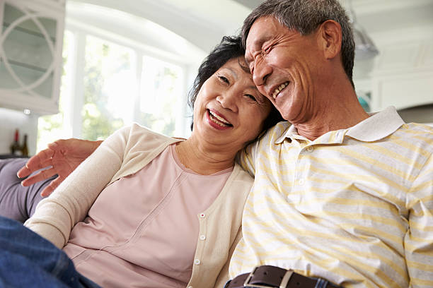 Senior Asian Couple At Home Relaxing On Sofa Together Senior Asian Couple At Home Relaxing On Sofa Together east asian ethnicity stock pictures, royalty-free photos & images