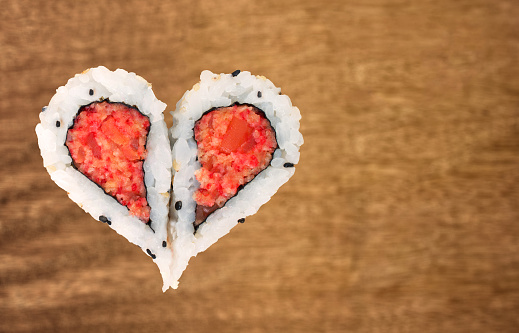 Two pieces of sushi forming the heart shape on a brown wooden background