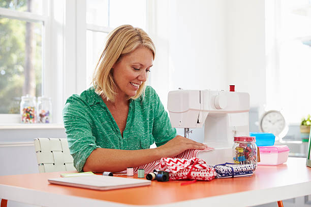 Woman Making Clothes Using Sewing Machine At Home Woman Making Clothes Using Sewing Machine At Home woman stitching stock pictures, royalty-free photos & images