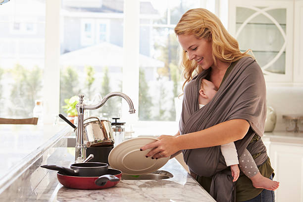 Busy Mother With Baby In Sling Multitasking At Home