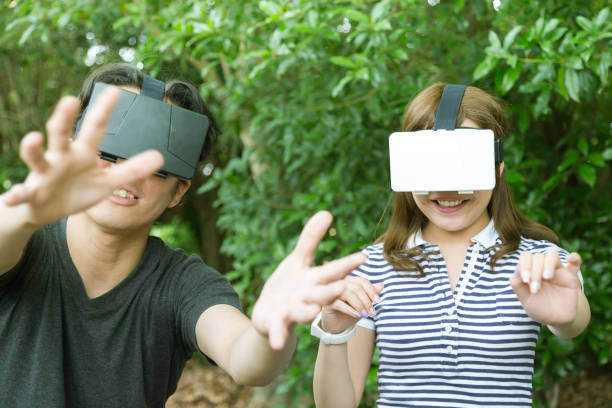 Friends having fun with Virtual Reality Consoles A young Japanese Couple Enjoying Virtual Reality Consoles at a park in Kyoto, Japan. head mounted display stock pictures, royalty-free photos & images