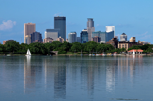 Downtown Minneapolis reflecting in Lake Calhoun including a sail boat and the marina with several moored sail boats.