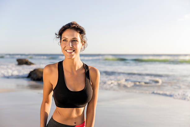 sportive jeune femme souriant sur la plage - brassière de sport photos et images de collection