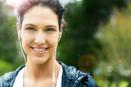 A photo of happy woman wearing earphones. Portrait of beautiful female is enjoying music. She is spending leisure time outdoors.