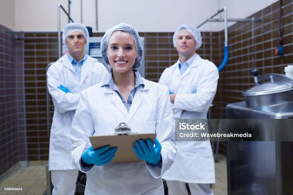 Girl holding a clipboard with these colleagues behind her Girl holding a clipboard with these colleagues behind her in the factory Hair Net Stock Photo