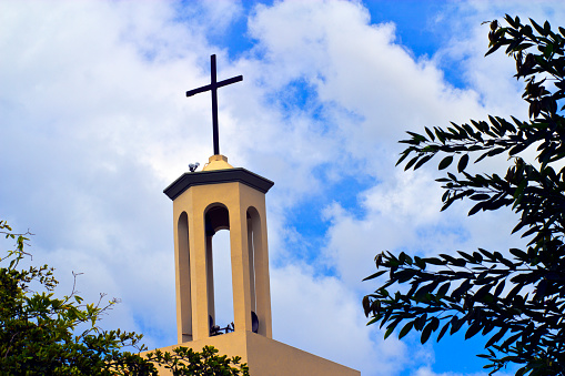 Church steeple and Christian cross with blue cloudy sky background.