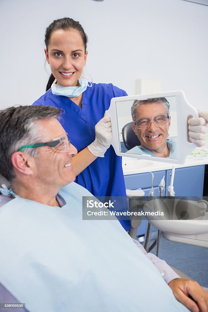 Smiling dentist showing teeth of her patient with a mirror Smiling dentist showing teeth of her patient with a mirror in dental clinic 20-24 Years Stock Photo