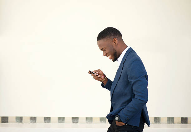 Smiling businessman walking and sending text message Side portrait of a smiling businessman walking and sending text message on mobile phone businessman african descent on the phone business person stock pictures, royalty-free photos & images