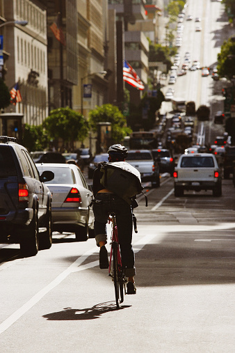 A male bike courier rides through traffic on a busy street in downtown San Francisco, California, USA.